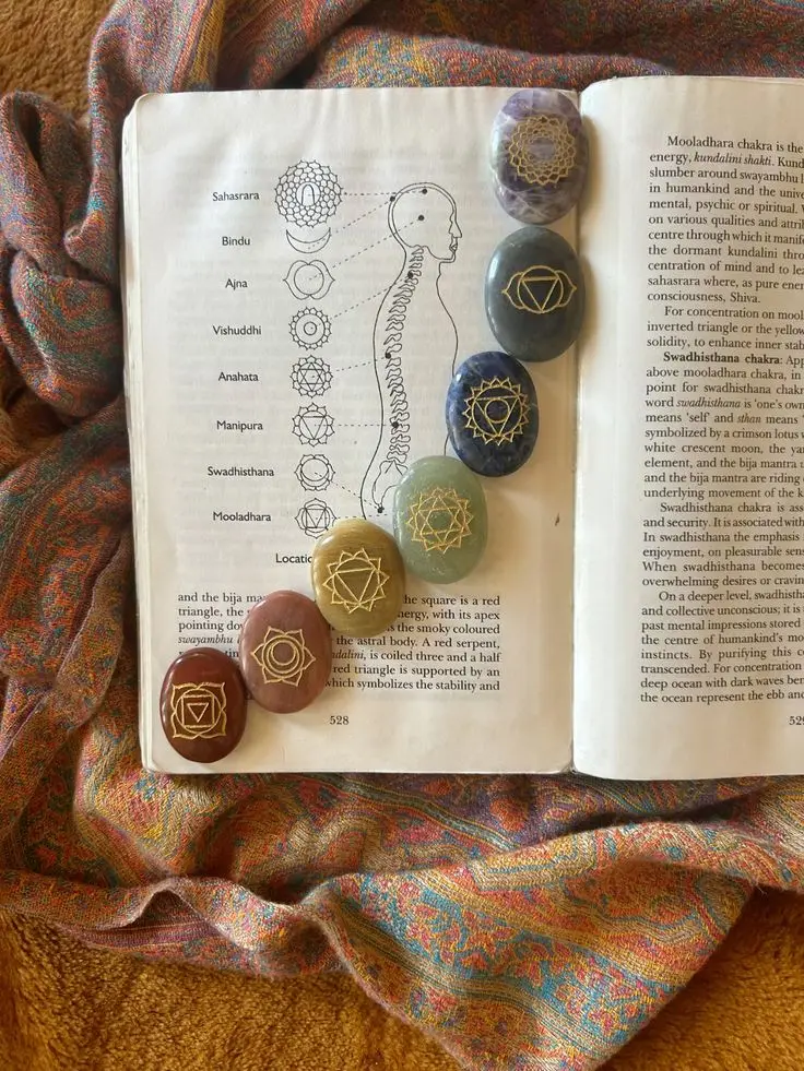 Livro aberto sobre os chakras, com sete pedras naturais e tecido de textura orgânica